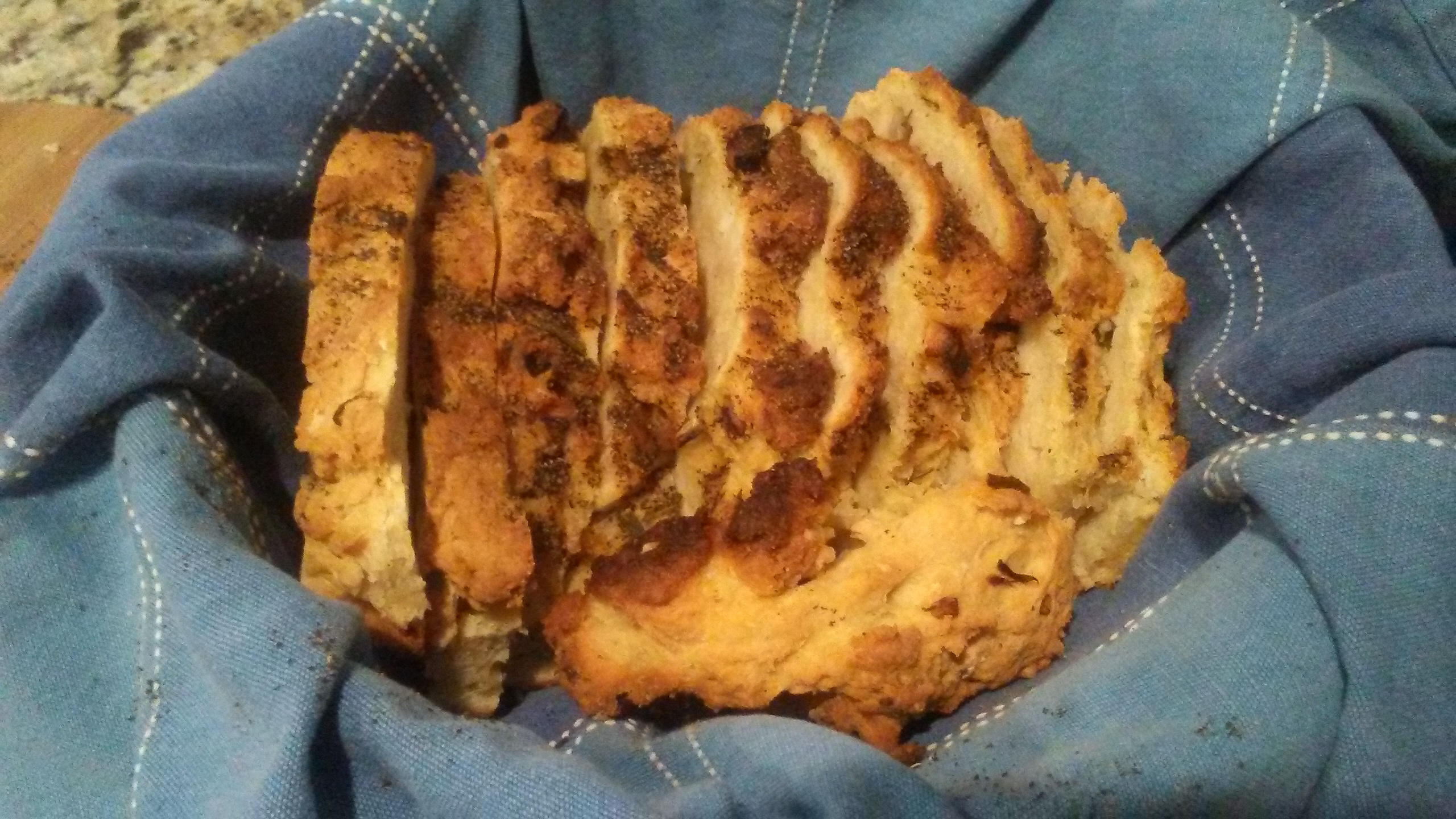 a somewhat flat, squashed-looking loaf of sliced herb-topped bread in a cloth-lined basket