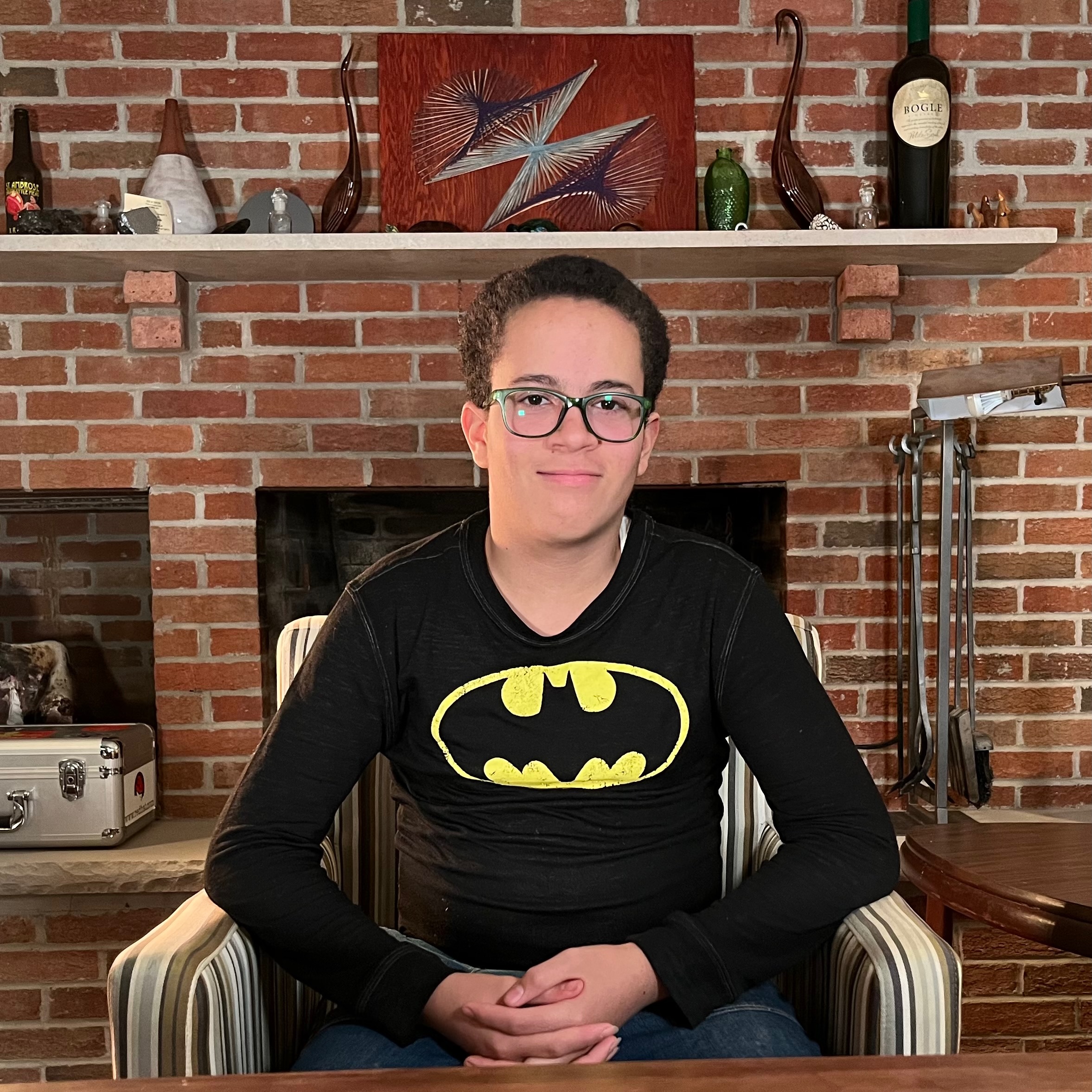 a portrait of a teenage boy seated at a table in front of a fireplace